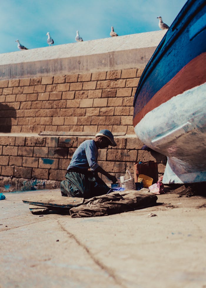A man paints a wooden boat near a brick wall, capturing a moment of maritime work and craftsmanship.